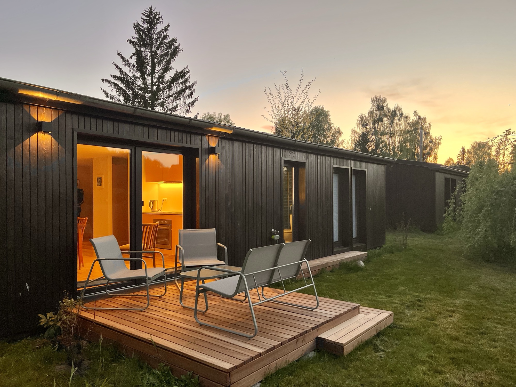 Haus 1 — Terrasse mit Sesseln vor dem beleuchteten Bungalow