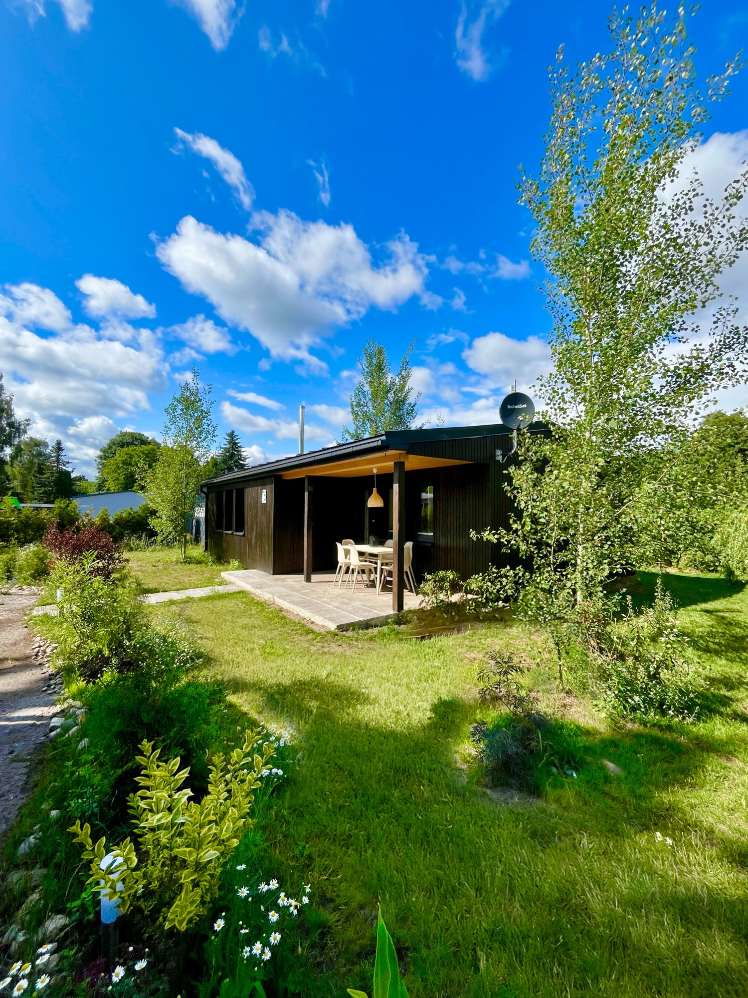 Haus 2 — Bungalow mit überdachter Veranda unter blauem Sommerhimmel